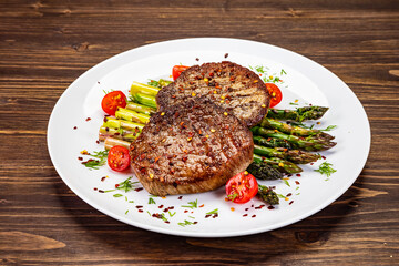 Barbecued beef steak with green asparagus on wooden table
