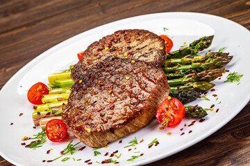 Barbecued beef steak with green asparagus on wooden table
