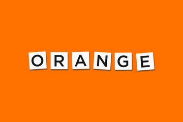 The word ORANGE, spelt with letter Scrabble tiles on a orange background