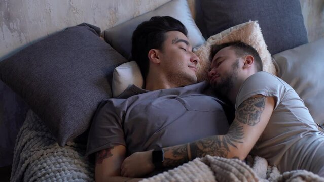 Young sweet couple have same-sex romance, embracing in bed kissing, passionate active man catches his boyfriend in caddle, honeymoon, LGBT concept.