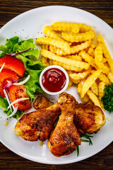 Barbecue chicken drumsticks with French fries, lettuce, tomatoes and ketchup on wooden table
