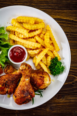 Barbecue chicken drumsticks with French fries, lettuce, tomatoes and ketchup on wooden table
