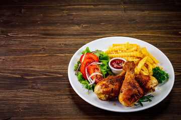 Barbecue chicken drumsticks with French fries, lettuce, tomatoes and ketchup on wooden table
