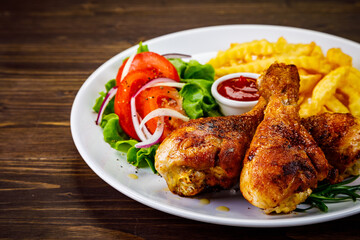 Barbecue chicken drumsticks with French fries, lettuce, tomatoes and ketchup on wooden table
