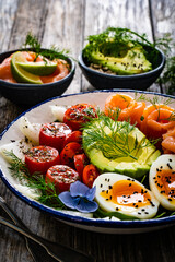 Salmon salad - smoked salmon, hard boiled eggs, avocado and leafy greens on wooden table
