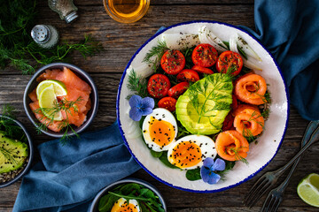 Salmon salad - smoked salmon, hard boiled eggs, avocado and leafy greens on wooden table
