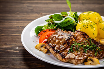 Fried beef steak with boiled potatoes and vegetables on wooden table
