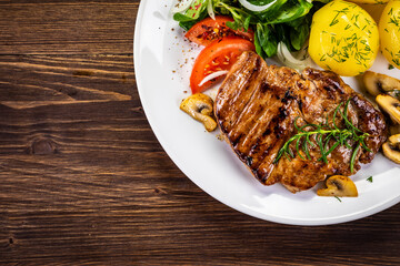 Fried beef steak with boiled potatoes and vegetables on wooden table
