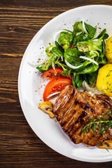 Fried beef steak with boiled potatoes and vegetables on wooden table
