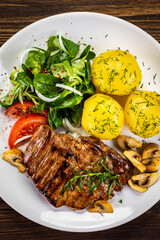 Fried beef steak with boiled potatoes and vegetables on wooden table
