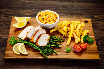 Sliced tasty roast chicken breast, green asparagus and cabbage on wooden table 
