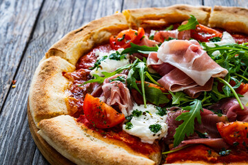 Pizza parma - prosciutto di parma, arugula, mozzarella, tomatoes, burrata on wooden table

