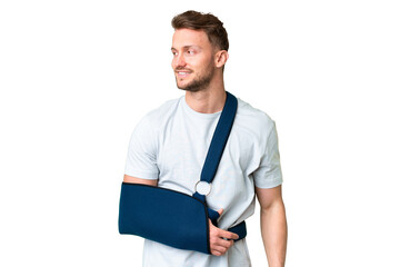 Young caucasian man with broken arm and wearing a sling over isolated chroma key background looking...