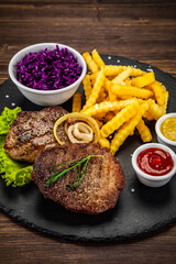 Fried beef sirloin with potatoes and vegetables on black stone plate on wooden table
