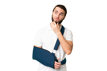 Young handsome man with broken arm and wearing a sling over isolated chroma key background having...