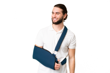 Young handsome man with broken arm and wearing a sling over isolated chroma key background looking to the side and smiling