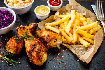 Barbecued chicken drumsticks with French fries, lettuce, tomatoes and ketchup on wooden table 