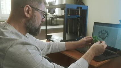 Male engineer with laptop inspecting 3d printed object in modern start up office. People, modern technology and contemporary business concept