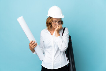 Young architect Georgian woman with helmet and holding blueprints over isolated background having doubts