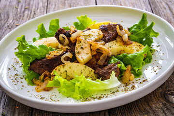 Fried liver with apples and onion on wooden table
