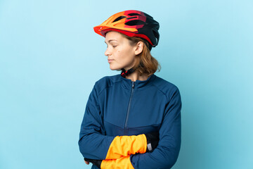 Young cyclist woman isolated on blue background looking to the side