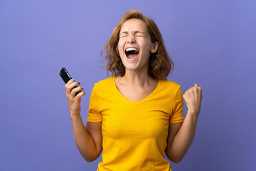 Young Georgian woman isolated on purple background using mobile phone and doing victory gesture