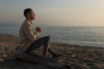 young man in a shirt, making a prayer in a sunset on the beach