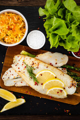 Fish dish - fried fish fillet with green asparagus and vegetables served on black stone plate on wooden table
