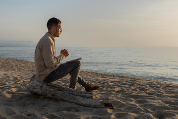 young man in a shirt, making a prayer in a sunset on the beach