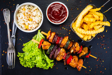 Chicken skewers - grilled meat with French fries on wooden background

