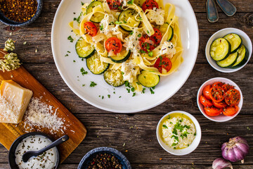 Tagliatelle with parmesan, zucchini, tomato and cream sauce on wooden table
