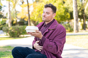 Fototapeta premium Young caucasian man at outdoors taking a box of takeaway food