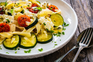 Tagliatelle with parmesan, zucchini, tomato and cream sauce on wooden table
