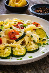 Tagliatelle with parmesan, zucchini, tomato and cream sauce on wooden table
