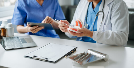 Dentist sitting at table with jaw samples tooth model and working with tablet and laptop in dental...