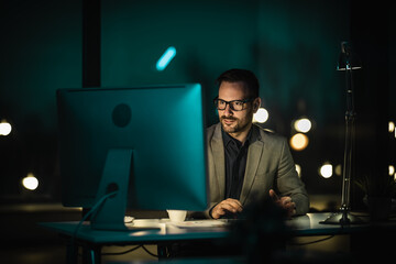 Portrait of tired young man working late at night at office with computer