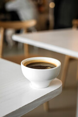 A white cup of black coffee americano on the edge of a table in a cafe
