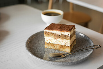 Tiramisu dessert cake and cup of black coffee at the table of a cafe