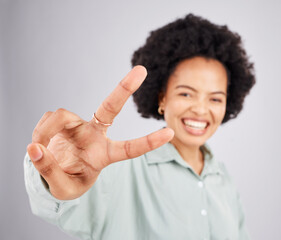 Portrait, peace and hand gesture with a woman in studio on a gray background feeling happy or carefree. Smile, emoji and sign with a happy young female indoor for freedom, wellness or good vibes