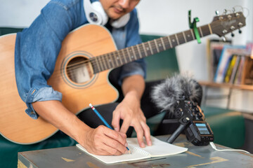 Man playing guitar and writing notes in a songbook at home Musician or composer writing a song or...