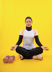 quiet Muslim woman wearing sportswear sit closing eyes during yoga on yellow background