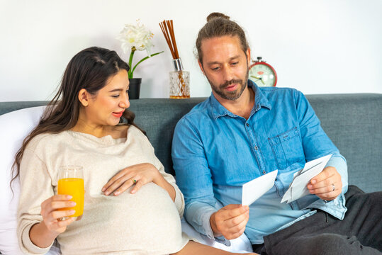 Caucasian pregnancy woman drinking orange juice during looking ultrasound photo of her newborn baby with husband on the bed in bedroom. Family relationship and pregnant maternity health care concept.