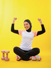 Smiling asian muslim woman in sportswear with raised hands on yellow background