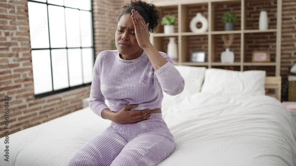 Poster African american woman suffering for stomach and headache sitting on bed at bedroom