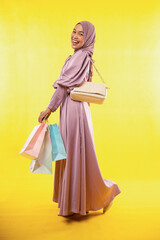 Asian woman in hijab dress laughing with shopping bag on yellow background