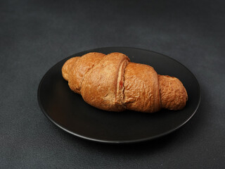 Delicious, freshly baked Croissant Lying on a black Plate against a black background