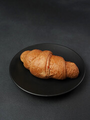 Delicious, freshly baked Croissant Lying on a black Plate against a black background