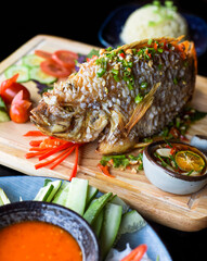 Red perch grilled in batter with vegetables and greens on wooden chop board isolated on black background side view