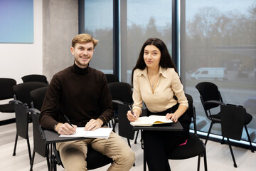 Smiling male and girl sitting on chairs in meeting room. Students studying, listening to lecture