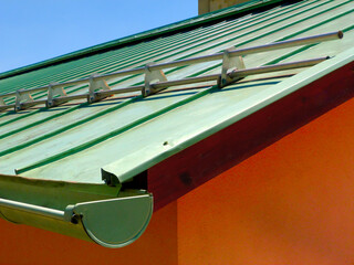 aged green weathered copper plate sloped roof. vertical seams. aluminum bar snow and ice breaker....